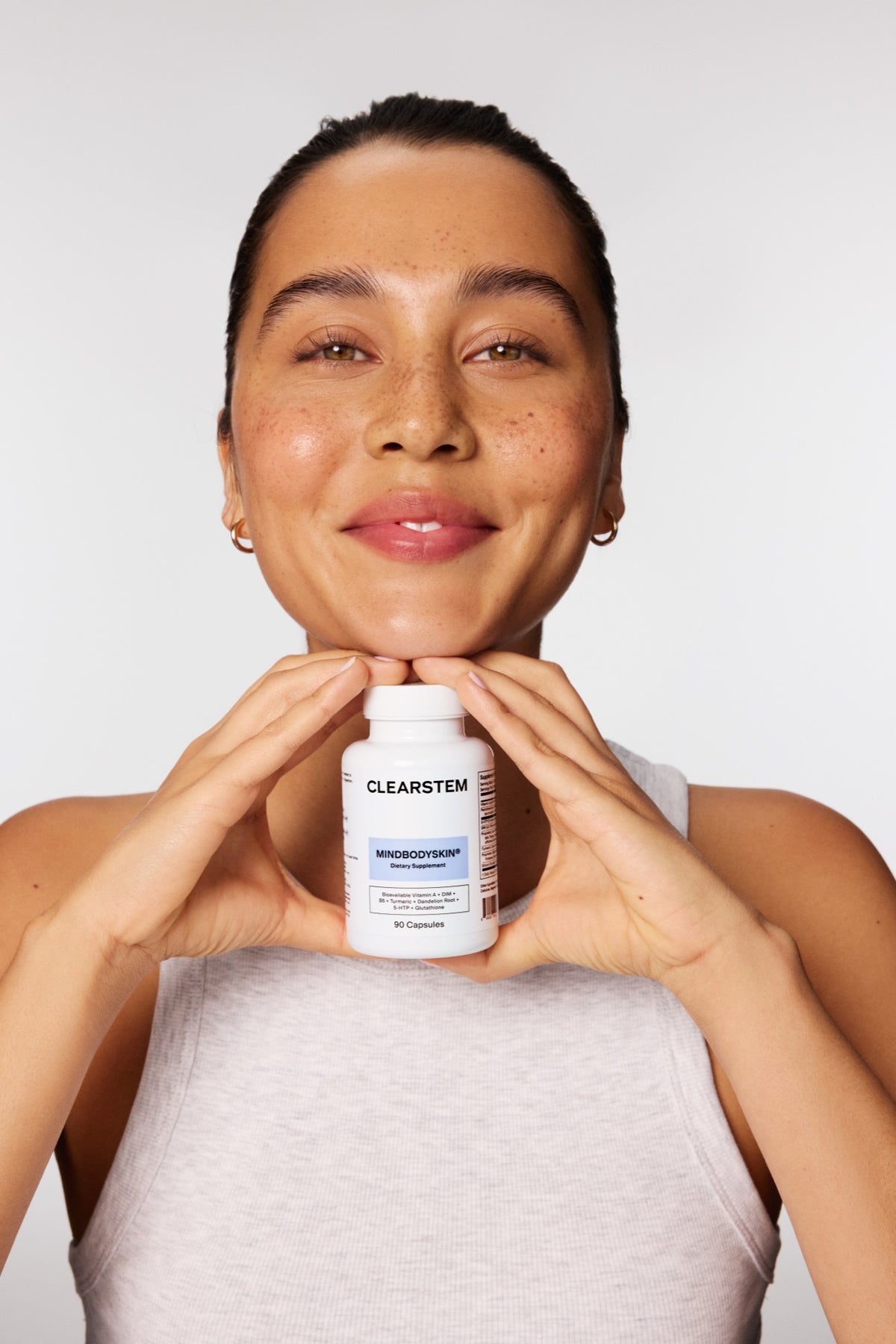 Smiling woman holding a MINDBODYSKIN® bottle under her chin